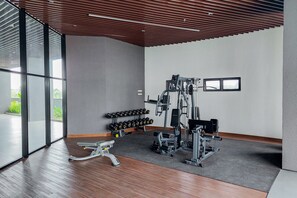 A modern gym with exercise equipment, a bench, and a rack of dumbbells. - Cozy 1BR at The Ayoma Apartment (South Tangerang)