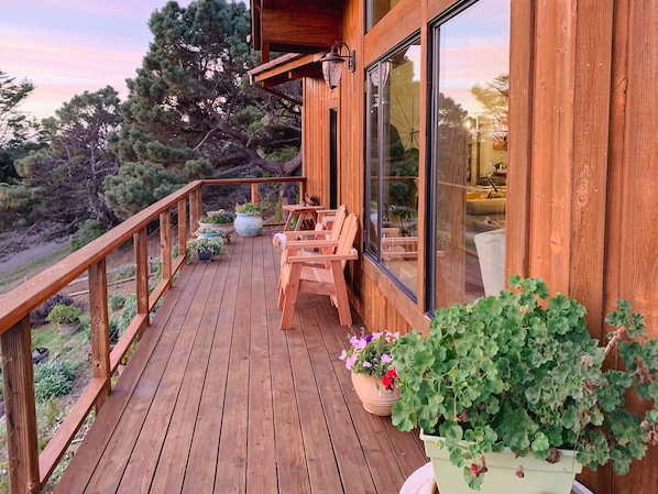 A wooden deck with chairs and potted plants, overlooking a forested area.