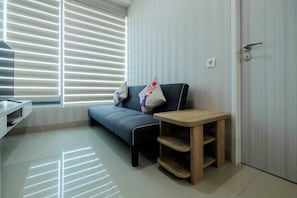 A modern living room with a sofa, a wooden side table, and a window with blinds.