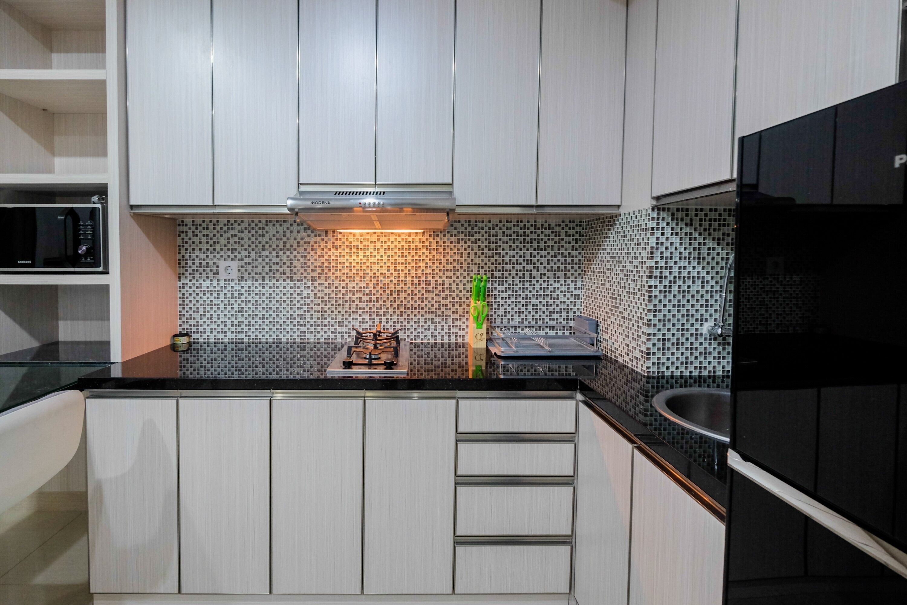 A modern kitchen with white cabinets, a black countertop, a microwave, and a tiled backsplash.