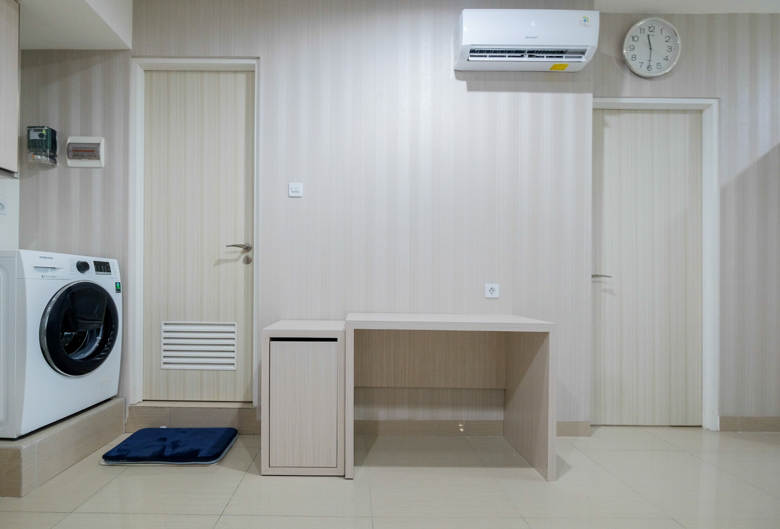 A laundry room with a washing machine, a drying rack, a desk, and a clock on the wall.