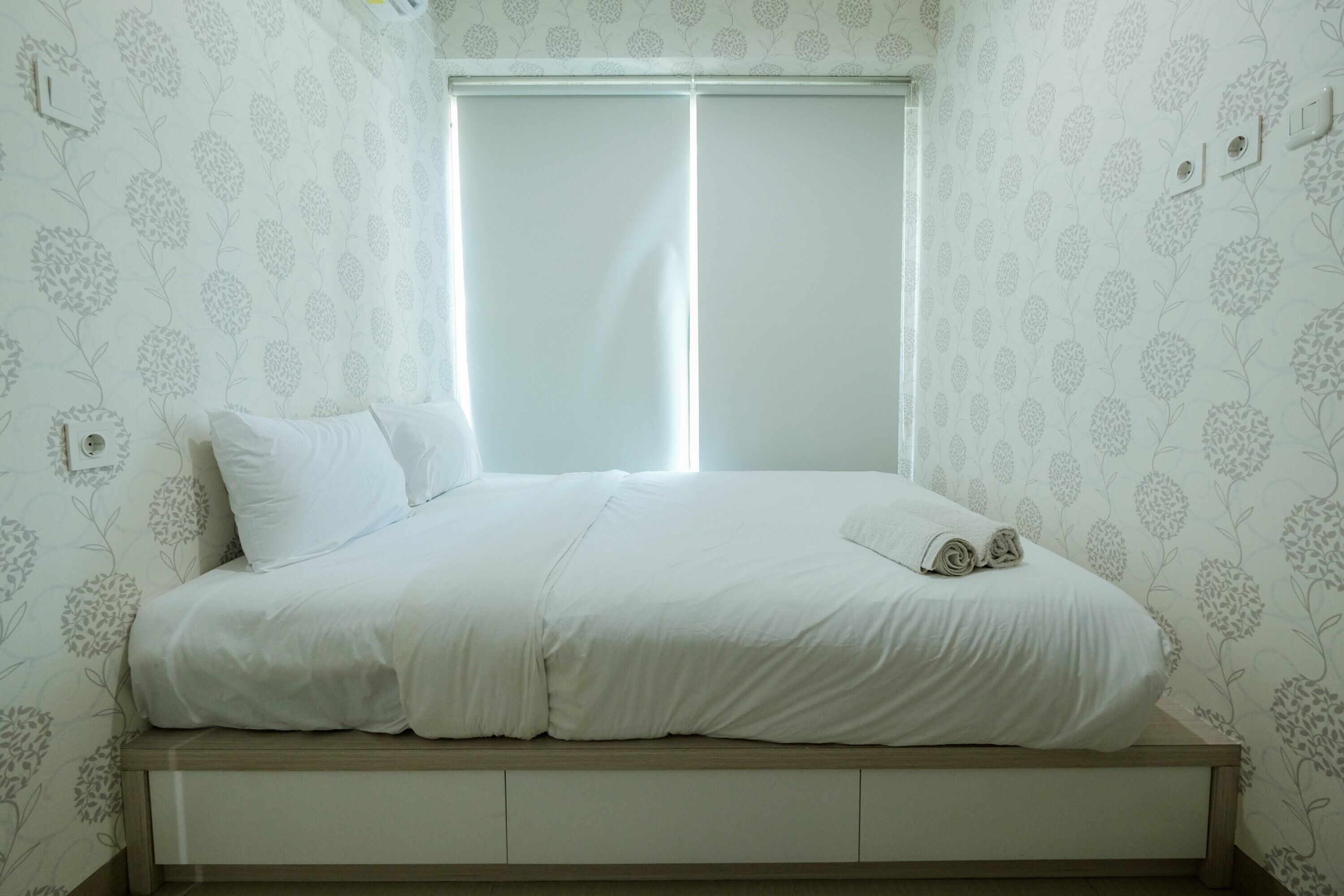 Un dormitorio con cama, ventana con persianas y pared con estampado floral.
