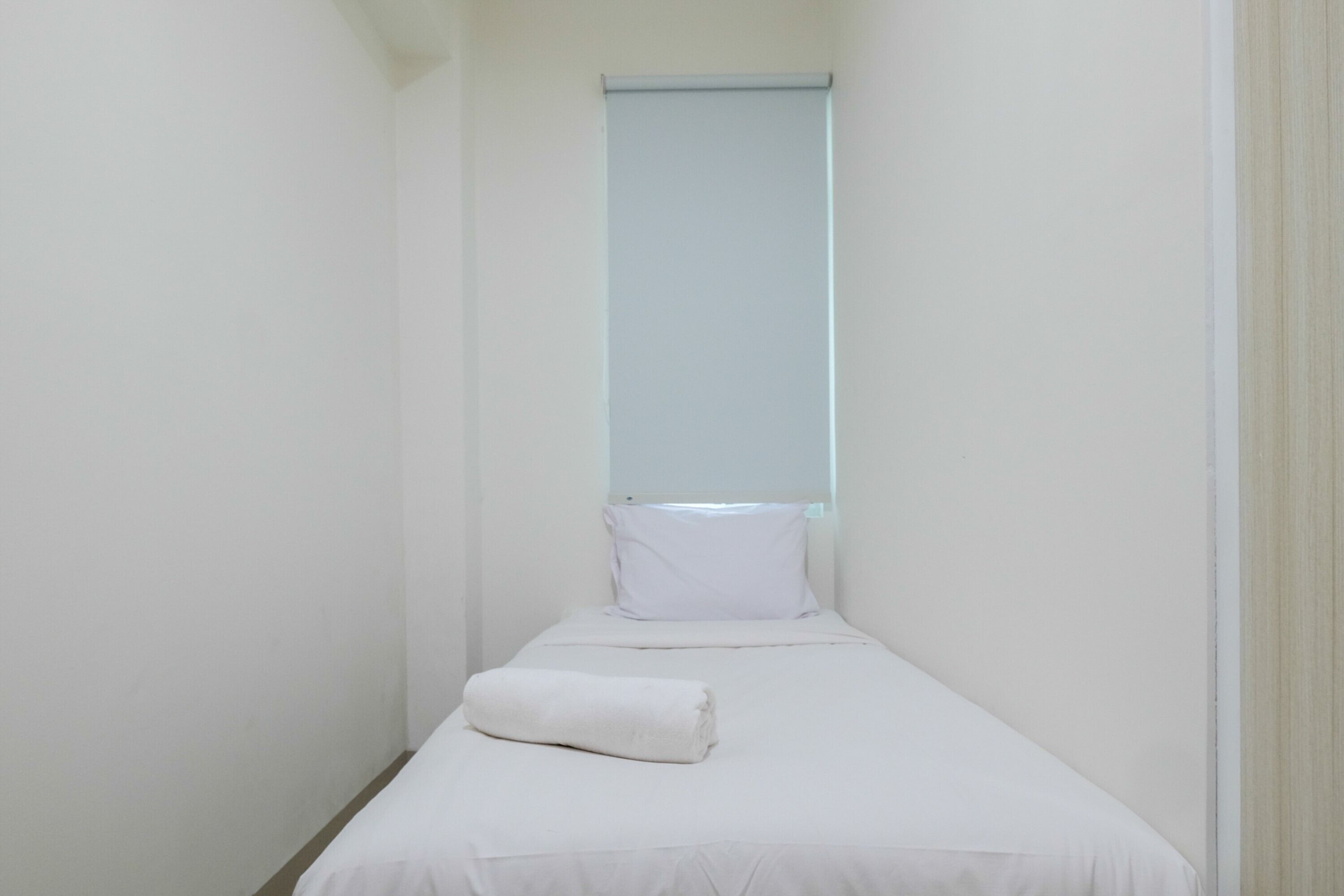 Une petite chambre d’hôtel étroite, avec un lit simple, une fenêtre et une serviette blanche posée sur le lit.