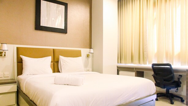 Ein Hotelzimmer mit einem großen Bett, einem Schreibtisch mit Stuhl und einem Fenster mit Vorhängen.
