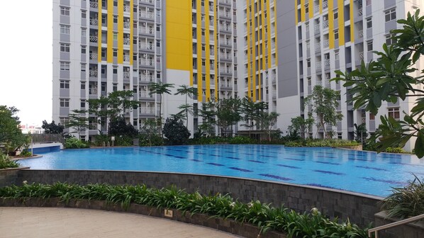 A swimming pool surrounded by greenery, with a high-rise building in the background. - Nice 2BR at Springlake Summarecon Bekasi Apartment (Bekasi)