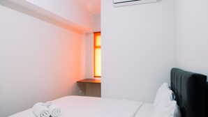 A hotel room with a bed, a wall-mounted air conditioner, and a window with a view of a sunset.