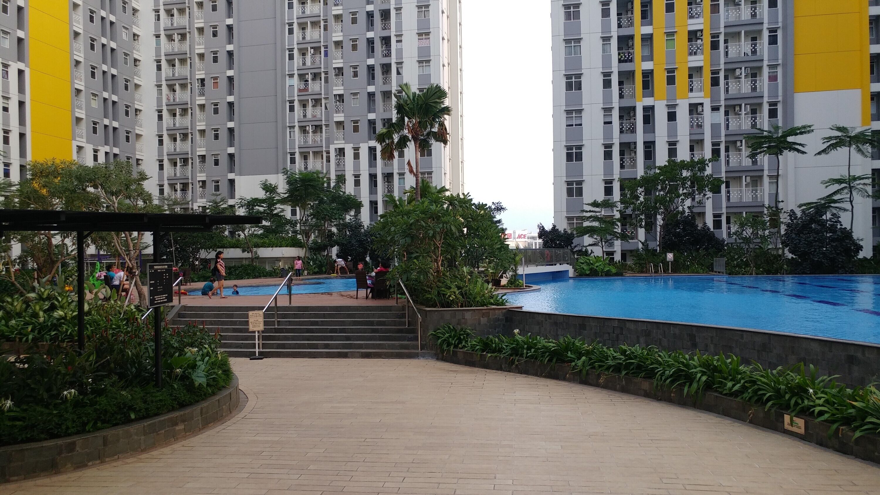 A residential building with a swimming pool, surrounded by greenery and a covered area with steps leading to the pool.