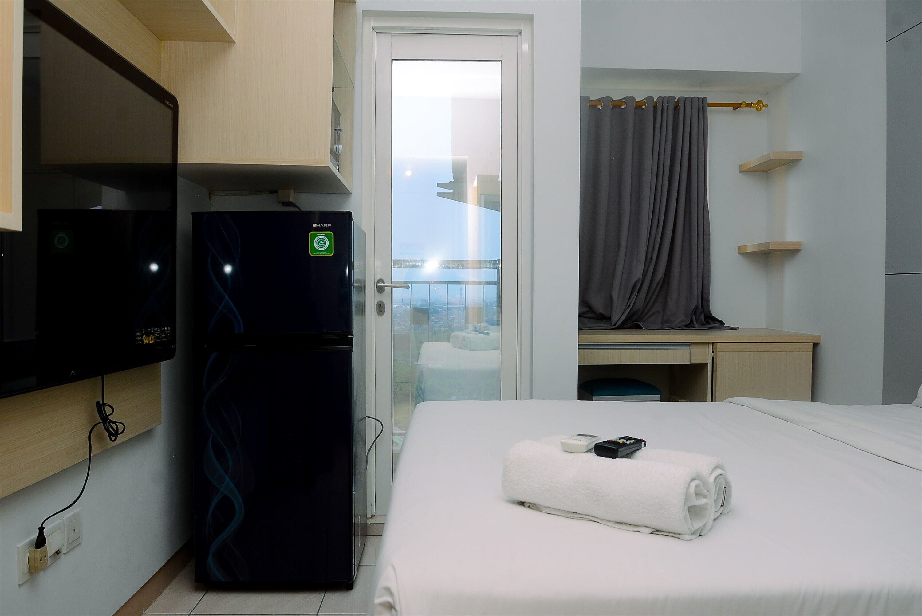 Habitación de hotel con cama, televisión, refrigerador, escritorio y balcón con vistas.