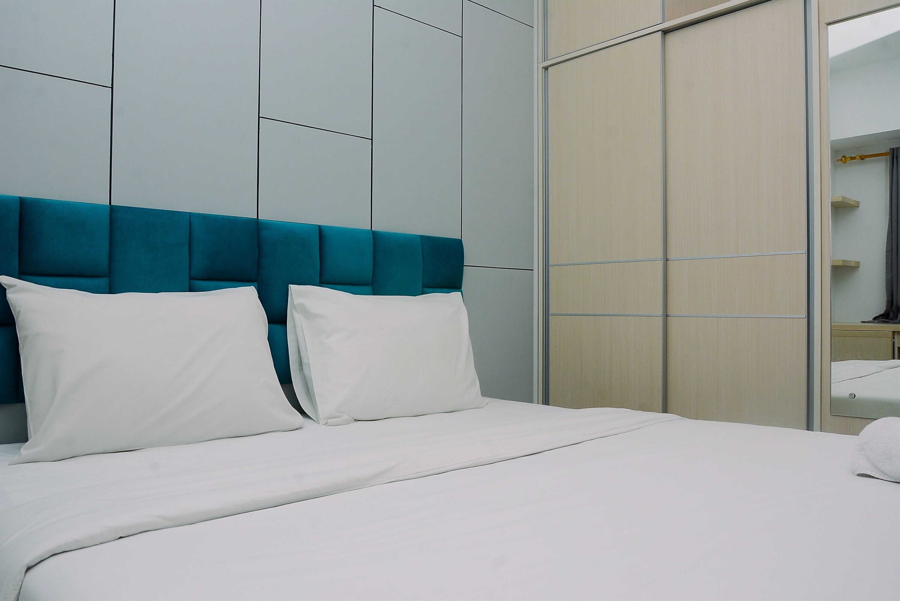 A hotel room with a bed, white bedding, a teal headboard, and a wardrobe with a mirror.