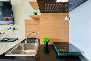 A modern kitchen with a stainless steel sink, a built-in induction cooktop, and a wall-mounted TV.