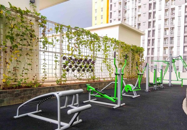 An outdoor gym area with exercise equipment, a climbing wall, and a building in the background.