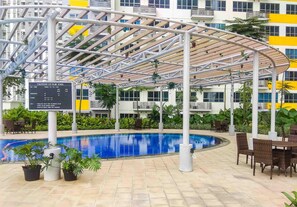 An indoor swimming pool with a covered seating area, surrounded by potted plants and a signboard.
