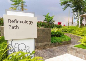 A sign reading 'Reflexology Path' in a landscaped area with plants and a pathway.