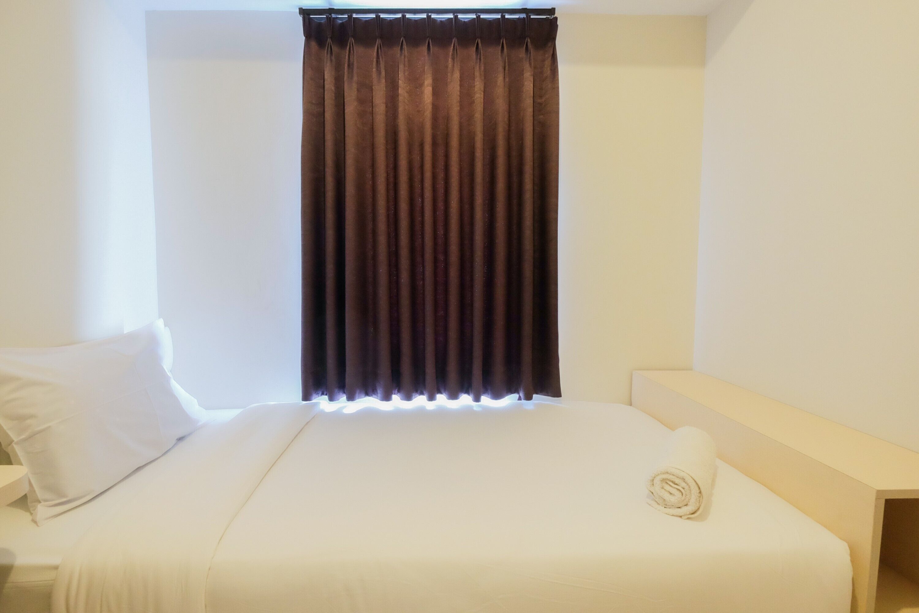 Un lit bien fait, avec des draps blancs, un rideau marron foncé et un oreiller blanc.