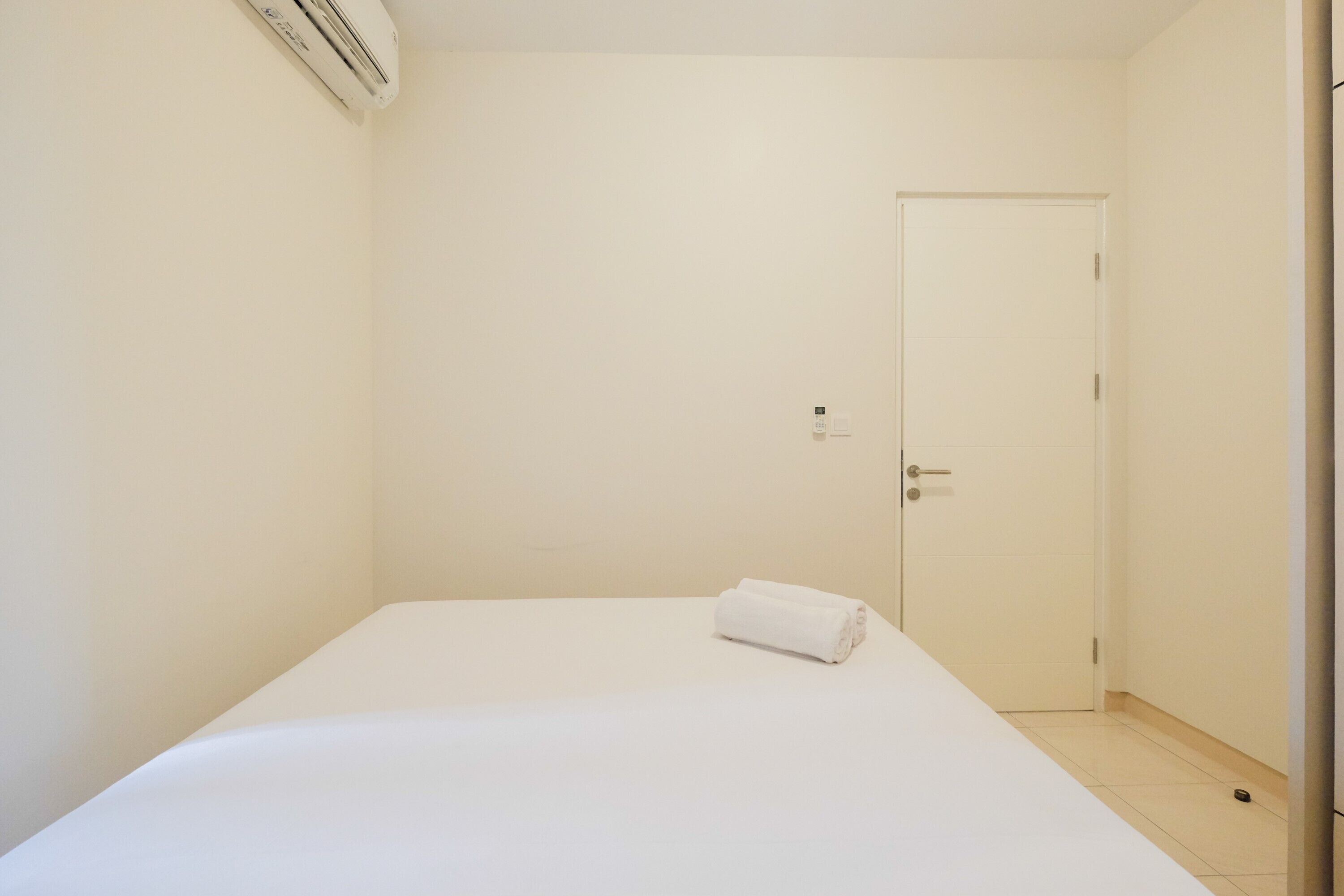 Une petite pièce propre, avec un lit simple, une porte et un appareil de climatisation.