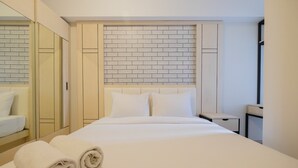A hotel room with a neatly made bed, a brick-patterned headboard, a large mirror, and a wardrobe. - Spacious 2BR Apartment at The Springlake Summarecon Bekasi (Bekasi)