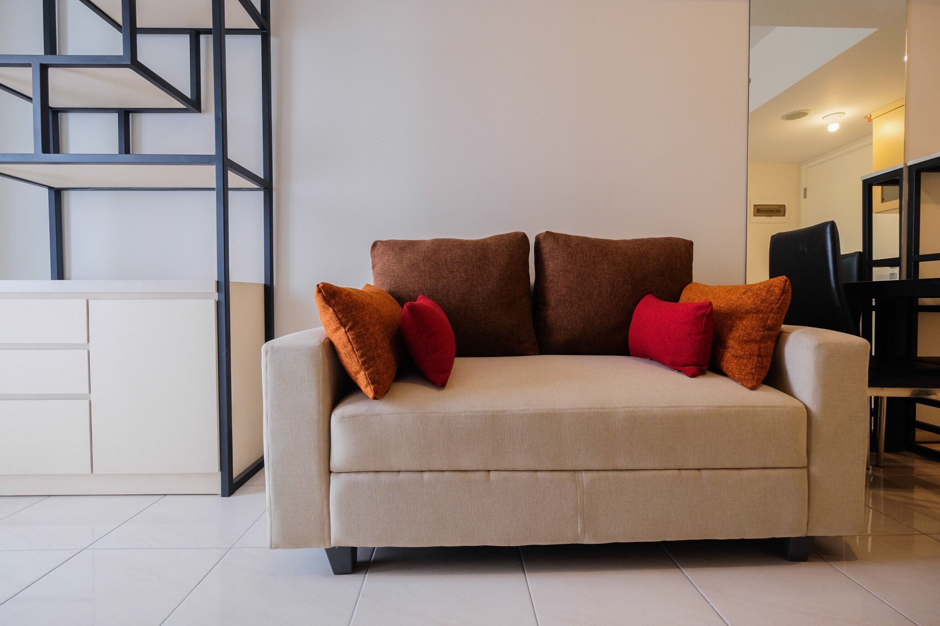 A modern living room with a beige sofa, two brown cushions, and red pillows.