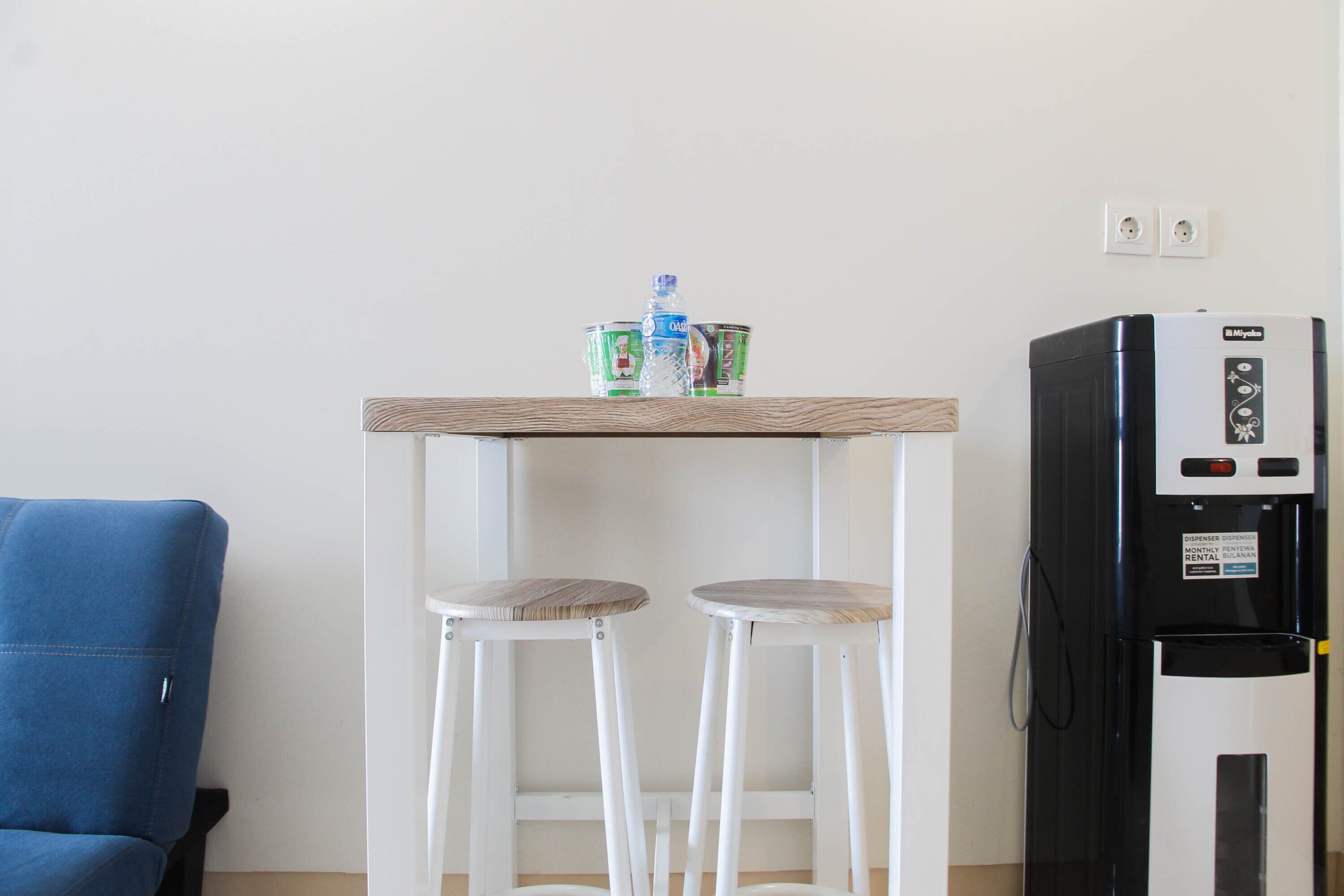 A kitchenette with a refrigerator, a wooden table with two stools, and a blue chair.