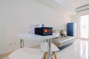 Une chambre d’hôtel moderne avec une table ronde blanche, un canapé et un mini-bar.