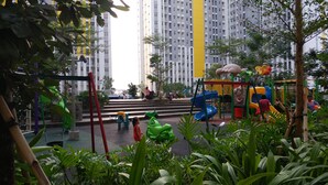 Un parque infantil con toboganes y estructuras para escalar, rodeado de vegetación y edificios altos.