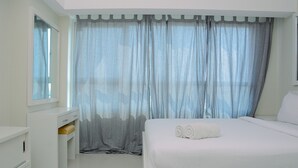 A bedroom with a bed, a bedside table, a mirror, and a window with curtains.