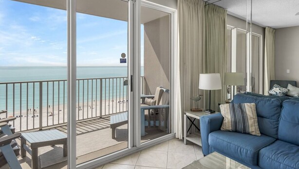 A balcony with a view of the beach and ocean, a blue sofa, and a small table with a lamp. - Majestic Sun A703*Gulf Views*Heated Pools/Hot Tubs*Beach Gear*Tennis (Destin)