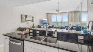 A modern kitchen with a large island, a dining area with blue sofas, and a balcony with a view of the sea. - Majestic Sun A703*Gulf Views*Heated Pools/Hot Tubs*Beach Gear*Tennis (Destin)
