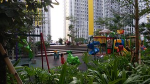 A playground with slides and climbing structures, surrounded by greenery and a multi-story building in the background. - Comfortable and Lovely 2BR Apartment at Springlake Summarecon (Bekasi)