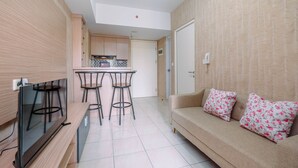 A modern living room with a flat-screen TV, a sofa with floral cushions, and a kitchen area with a bar stool and tiled backsplash. - Comfortable and Lovely 2BR Apartment at Springlake Summarecon (Bekasi)
