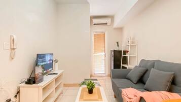 A modern living room with a grey sofa, a small coffee table, a TV on a wooden stand, and a plant on the table.
