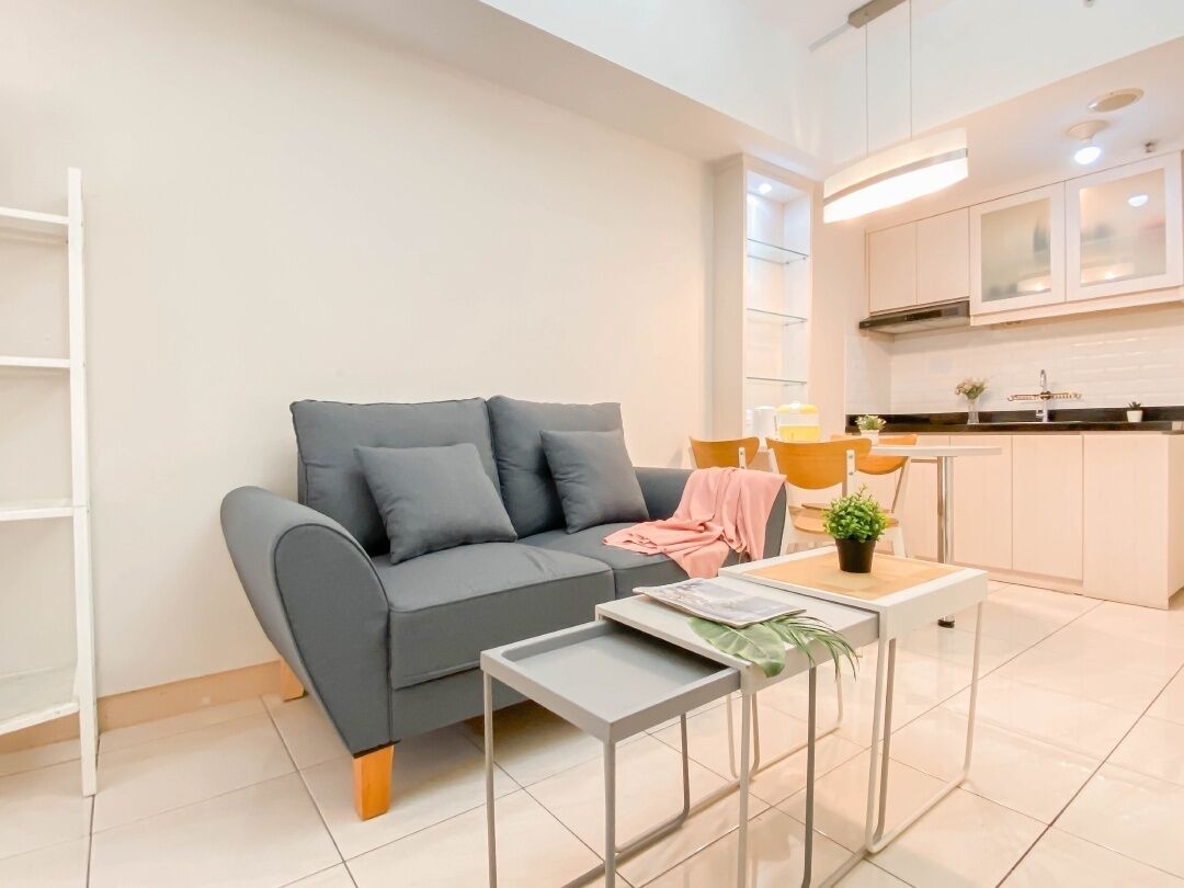 A modern living room with a grey sofa, a small side table, and a kitchen area with white cabinets and a countertop.