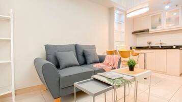 A modern living room with a grey sofa, a small side table, and a kitchen area with white cabinets and a countertop.