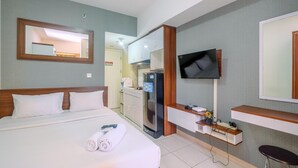 A hotel room with a bed, a TV mounted on the wall, a small kitchenette, and a mirror above the bed. - Elegant and Nice Studio at Springlake Sumarecon Apartment (Bekasi)