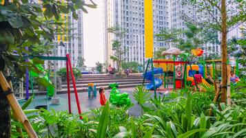 A playground with slides and climbing structures surrounded by greenery and tall buildings.