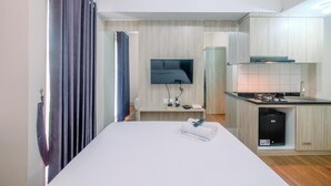Ein Hotelzimmer mit Bett, Wand-Fernseher, einer kleinen Küchenzeile inklusive Spüle und Herd sowie einem durch einen Vorhang abgetrennten Badezimmer.