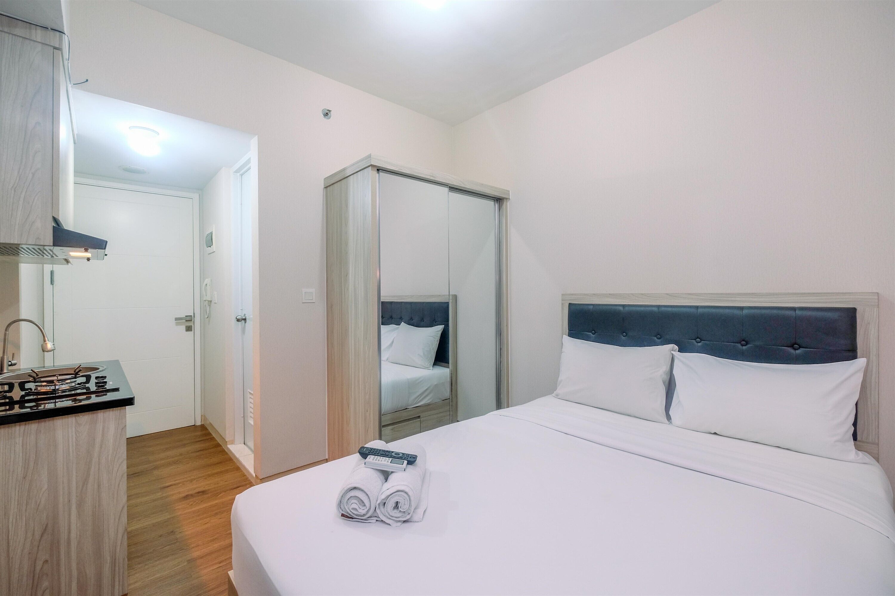 A hotel room with a bed, a mirror, a wardrobe, and a kitchenette.