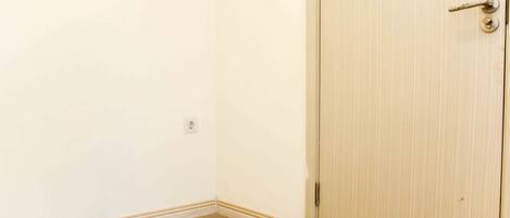 Una habitación con la puerta cerrada, un interruptor de luz en la pared y un objeto pequeño en el suelo.