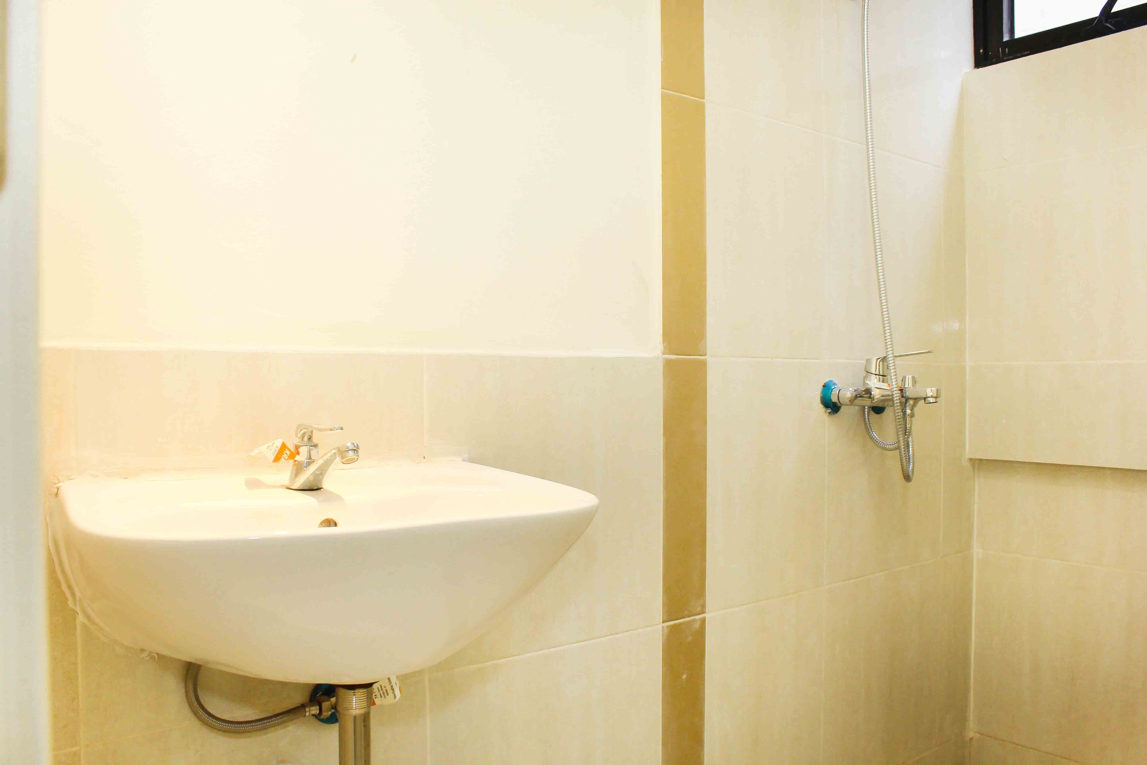 Ein Badezimmer mit einem weißen Waschbecken, einer Dusche und beige gefliesten Wänden.