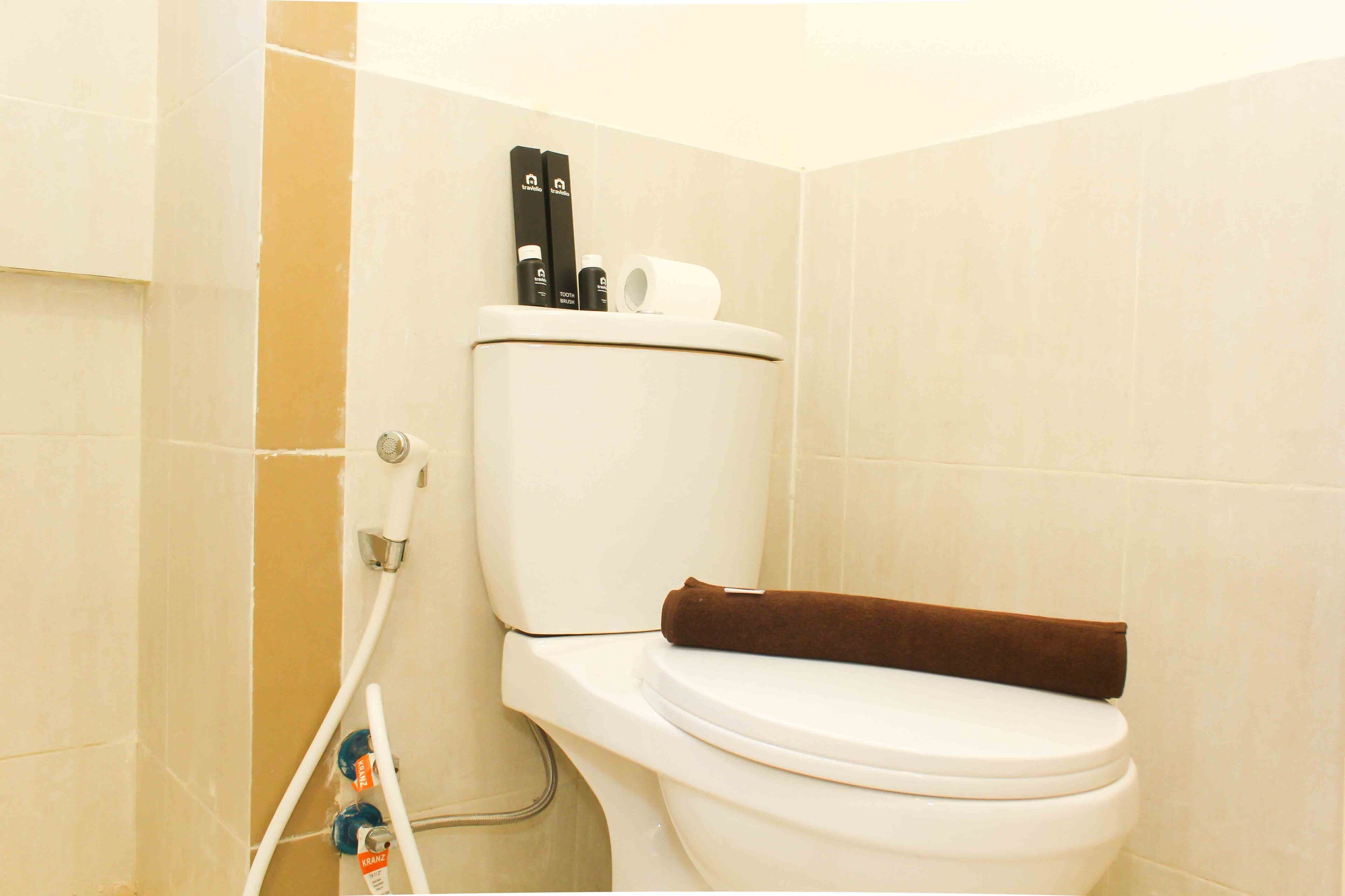 Un inodoro blanco con una toalla marrón sobre el asiento, un sujetarrollos y un calentador de agua.