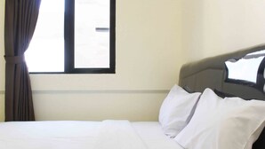 Ett hotellrum med en säng, vita sängkläder, en sänggavel och ett fönster med gardiner.
