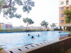 Una piscina con gente nadando, rodeada de edificios y árboles.