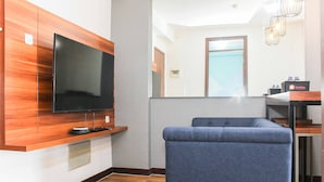 A modern living room with a flat-screen TV, a blue sofa, wooden paneling, a small table, and a mirror. - Homey and Simply 2BR at Lagoon Bekasi Town Square Apartment (Bekasi)
