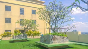 A rooftop garden with artificial grass, two large planters, and a building in the background. - Homey and Simply 2BR at Lagoon Bekasi Town Square Apartment (Bekasi)