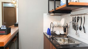 A modern kitchen with a black countertop, stainless steel sink, and a dish rack. There are utensils hanging on the wall and a travel food box on the counter. - Homey and Simply 2BR at Lagoon Bekasi Town Square Apartment (Bekasi)