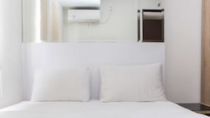 A hotel room with a bed, a nightstand, a mirror, and a wall-mounted air conditioning unit. - Homey and Simply 2BR at Lagoon Bekasi Town Square Apartment (Bekasi)