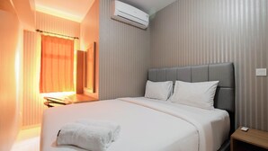 A hotel room with a large bed, a bedside table, a nightstand, an air conditioning unit, and a window with curtains. - Relaxing 2BR Apartment at The Springlake Summarecon (Bekasi)