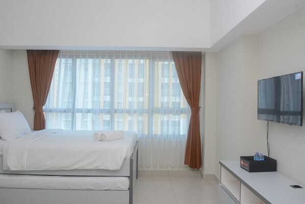 A modern hotel room with a bed, a TV, and a small table with a box of bottled water.