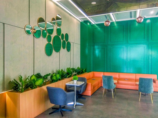 Un hall d’entrée moderne agrémenté d’un mur d’accent vert, d’un espace salon avec des canapés orange et d’un comptoir d’accueil avec des chaises bleues.
