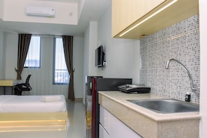 Une chambre d’hôtel moderne équipée d’un lit, d’un bureau, d’un téléviseur à écran plat, d’un coin cuisine avec un évier et d’une fenêtre avec des rideaux.