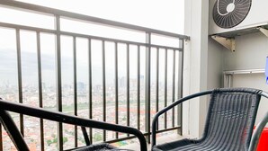 A balcony with a glass table, two wicker chairs, a white ashtray, and a city view.